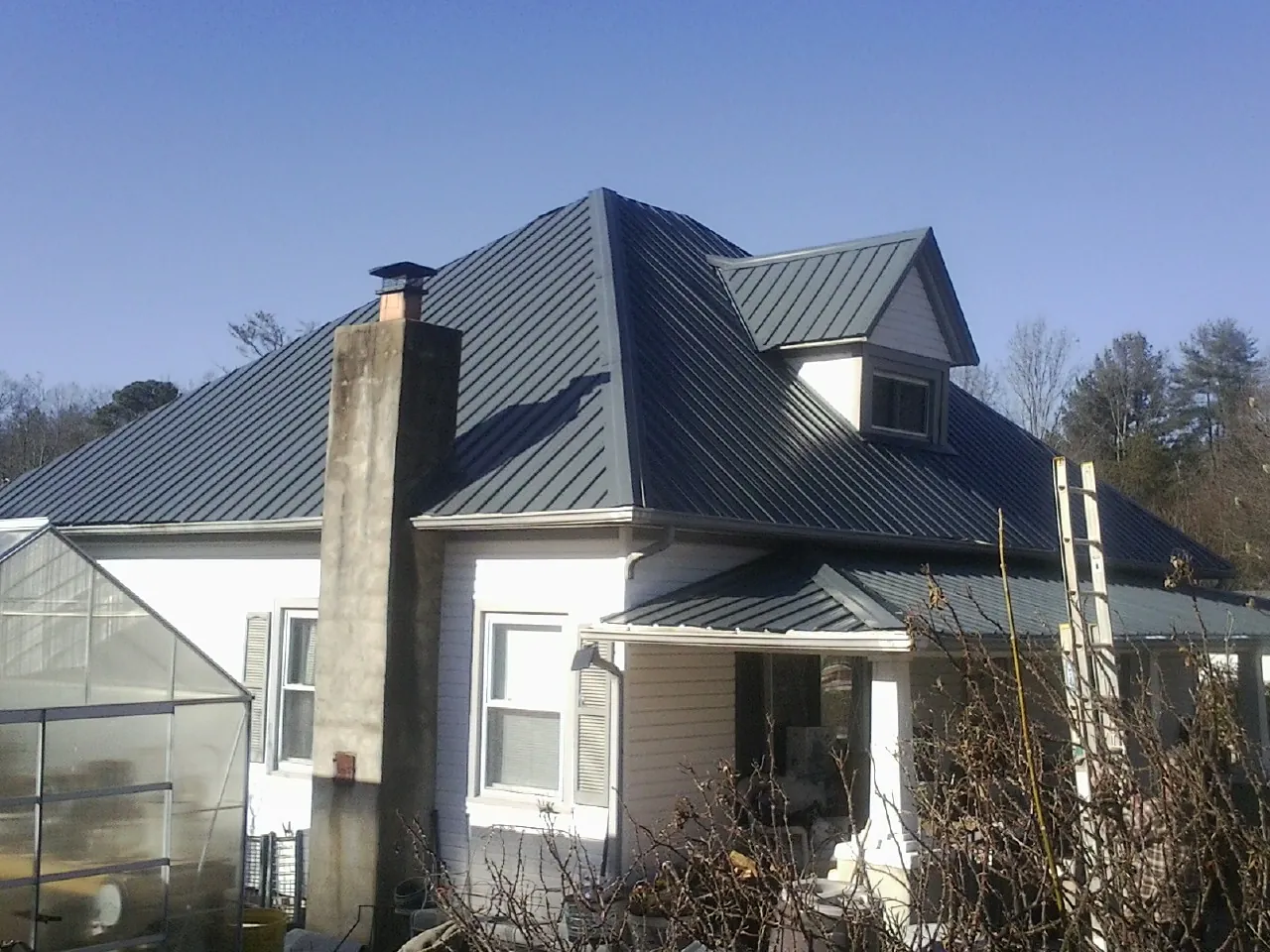 Dark blue standing seam metal roof on a white farmhouse with dormer — Slate & Tile Roof Repair by Roofing Brothers in Donalds