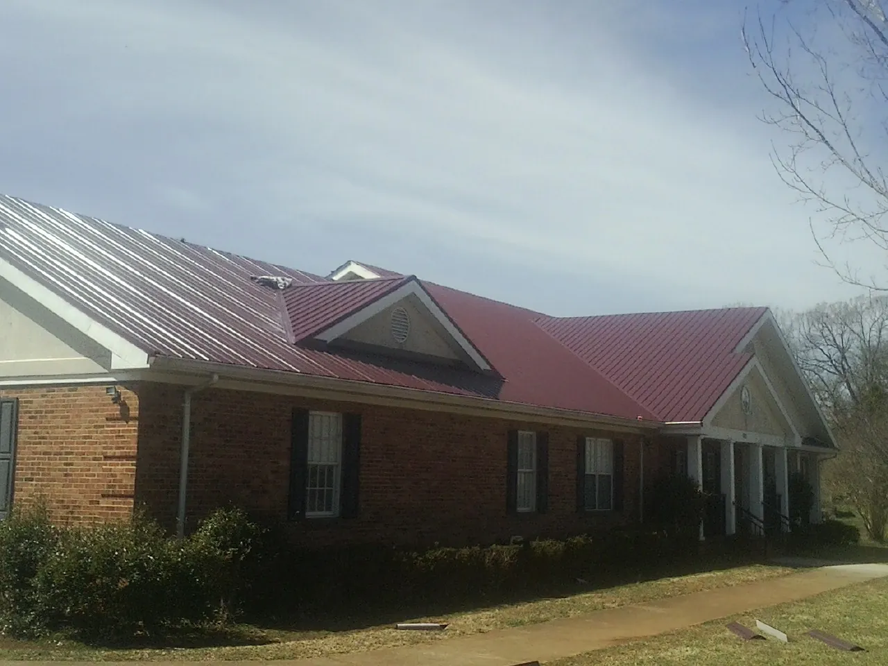 Red metal roof with gabled entries on a long brick building, from a Hail Damage Roof Repair job in Donalds