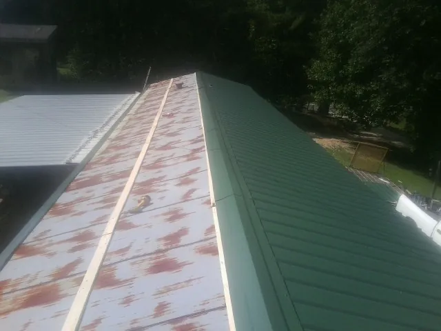 Old rusted panels beside newly installed green metal roofing — Wind Damage Roof Repair by Roofing Brothers in Donalds