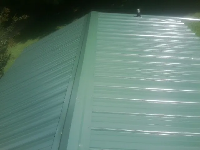 New green metal panels meeting at the ridge of a roof — Flat Roof Repair work by our crew in Donalds