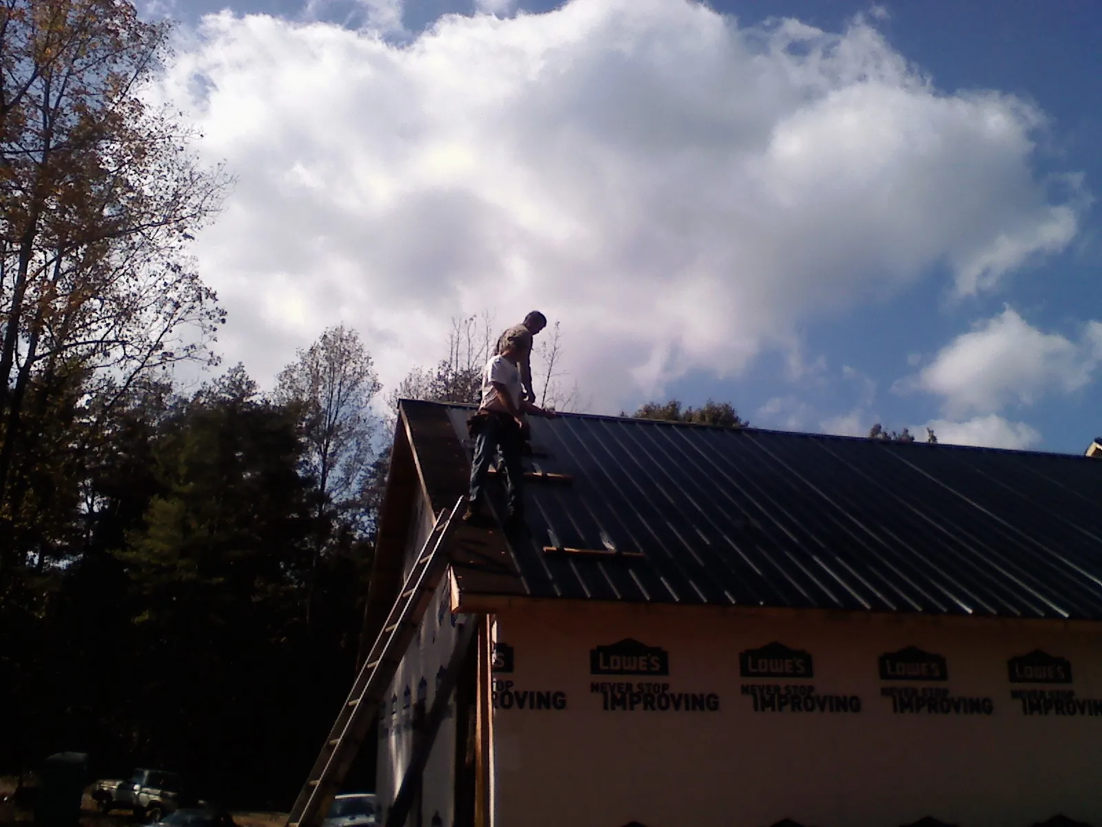 Roofer fastening dark metal panels high against a cloudy sky, from a Roof Inspection job in Donalds