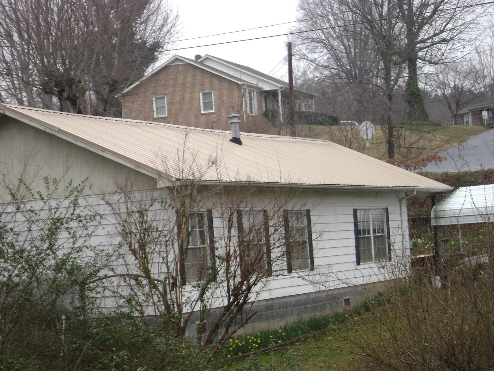 Tan metal roof on a white sided house set into a hillside — Commercial Roofing by Roofing Brothers in Donalds