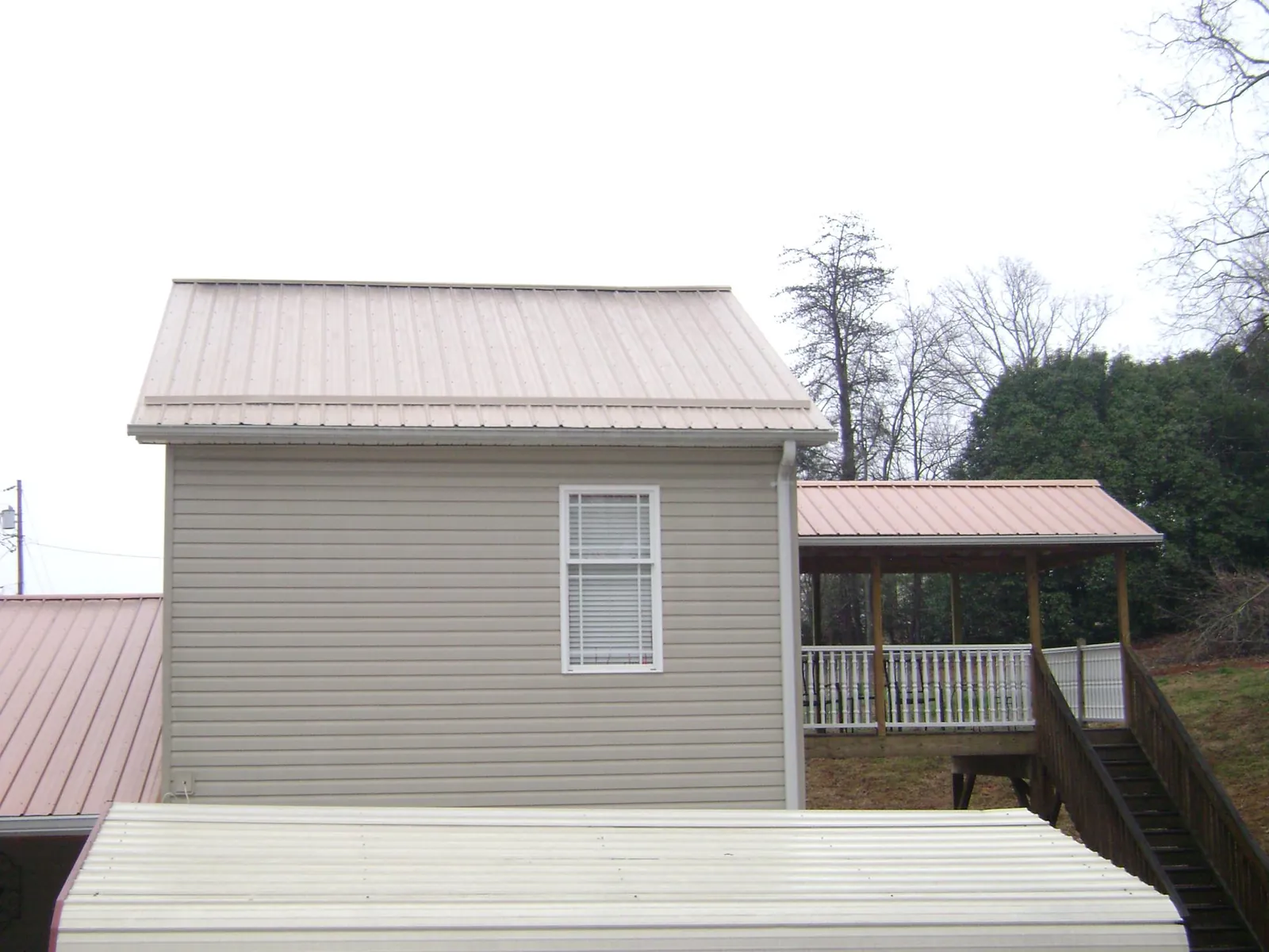 Tan metal roofs on a two story addition and attached porch, from a Roof Replacement job in Donalds